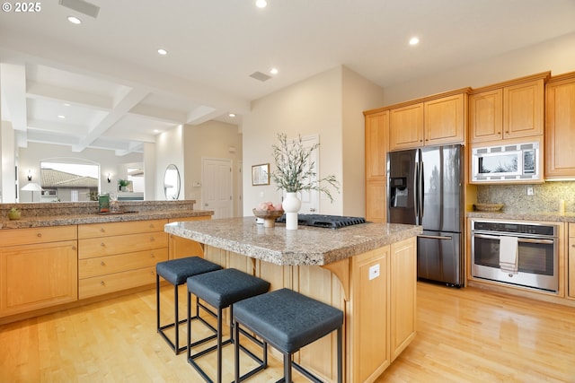 kitchen with a kitchen bar, a kitchen island, light hardwood / wood-style floors, and appliances with stainless steel finishes