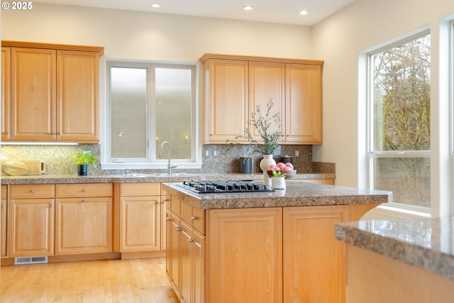 kitchen featuring sink, backsplash, stainless steel gas cooktop, light brown cabinets, and light wood-type flooring