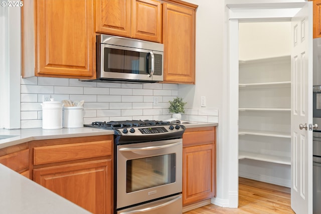 10540 SW Lancaster Rd, Portland, OR 97219 - kitchen with appliances with stainless steel finishes, light countertops, backsplash, light wood-type flooring, and brown cabinets