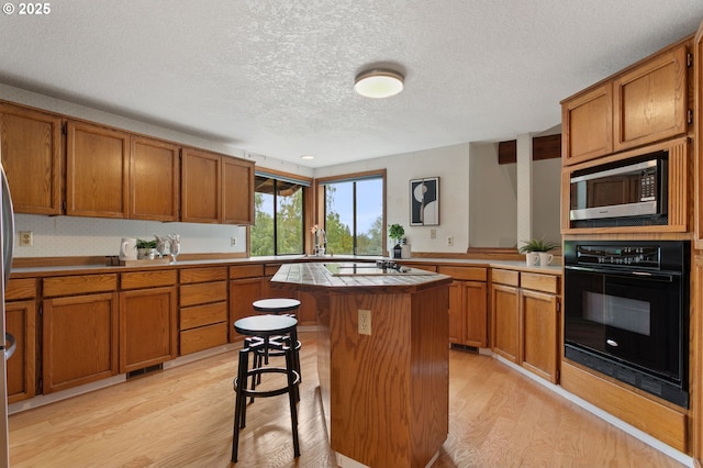 10315 SW 28th Ave, Portland, OR 97219 - kitchen with black oven, stainless steel microwave, light wood-style floors, a textured ceiling, and brown cabinetry