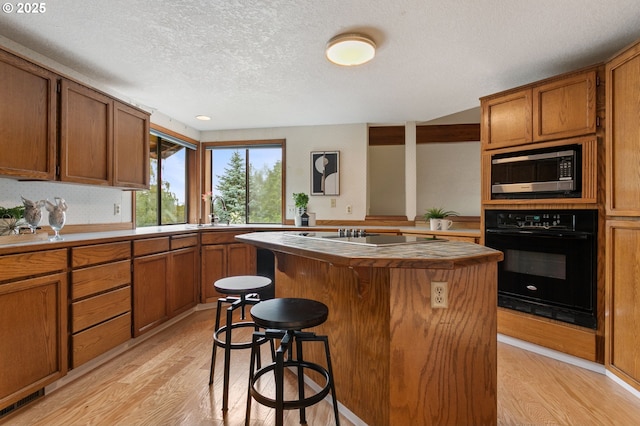 10315 SW 28th Ave, Portland, OR 97219 - kitchen featuring black appliances, light wood finished floors, a textured ceiling, a center island, and a kitchen breakfast bar