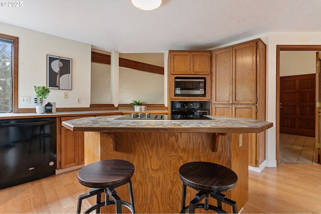 10315 SW 28th Ave, Portland, OR 97219 - kitchen featuring black appliances, tile counters, wallpapered walls, a kitchen bar, and light wood-style floors