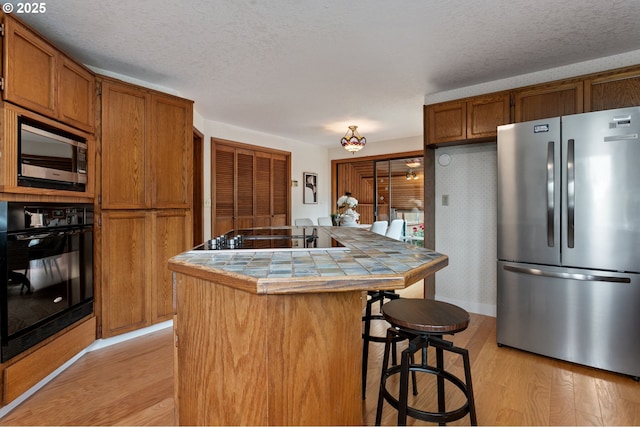 10315 SW 28th Ave, Portland, OR 97219 - kitchen featuring black appliances, tile countertops, light wood-style flooring, a kitchen bar, and brown cabinets