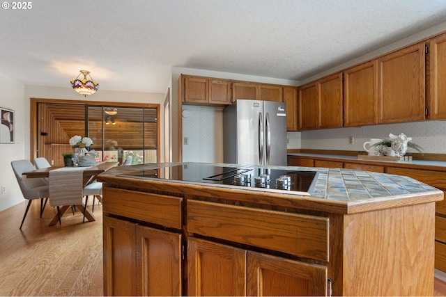 10315 SW 28th Ave, Portland, OR 97219 - kitchen featuring freestanding refrigerator, tile countertops, black electric cooktop, light wood-type flooring, and brown cabinets
