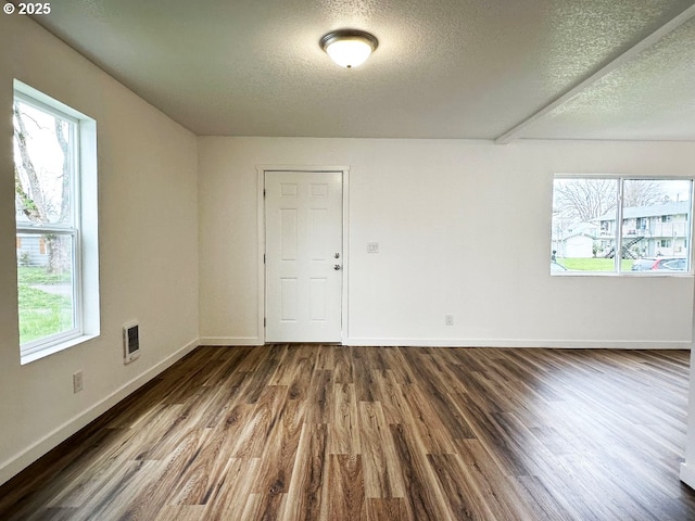 spare room featuring visible vents, plenty of natural light, and dark wood-type flooring