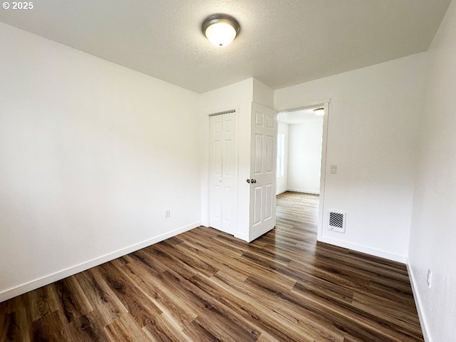 unfurnished room featuring a textured ceiling, dark wood-style floors, visible vents, and baseboards