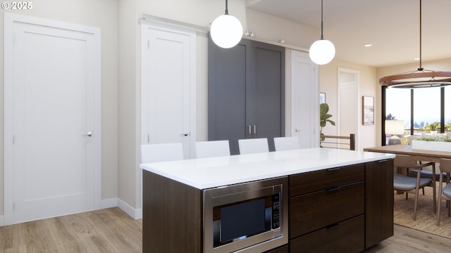 kitchen featuring dark brown cabinets, pendant lighting, stainless steel microwave, and light hardwood / wood-style flooring