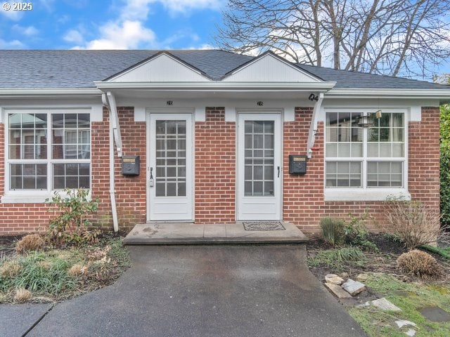 view of exterior entry with brick siding and a shingled roof