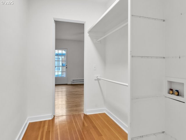 spacious closet with light wood-style floors and a baseboard radiator