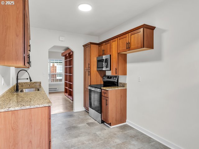 kitchen featuring brown cabinetry, light stone countertops, arched walkways, a sink, and stainless steel appliances