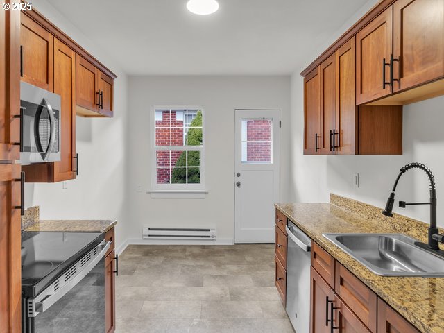 kitchen with a baseboard heating unit, light stone counters, brown cabinetry, stainless steel appliances, and a sink