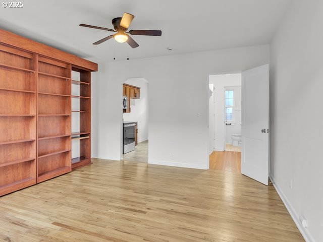 unfurnished room with baseboards, arched walkways, ceiling fan, and light wood finished floors