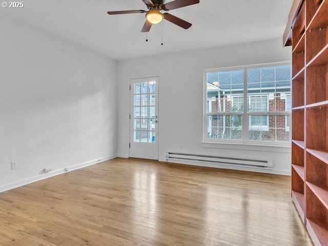 spare room with a ceiling fan, wood finished floors, baseboards, and baseboard heating