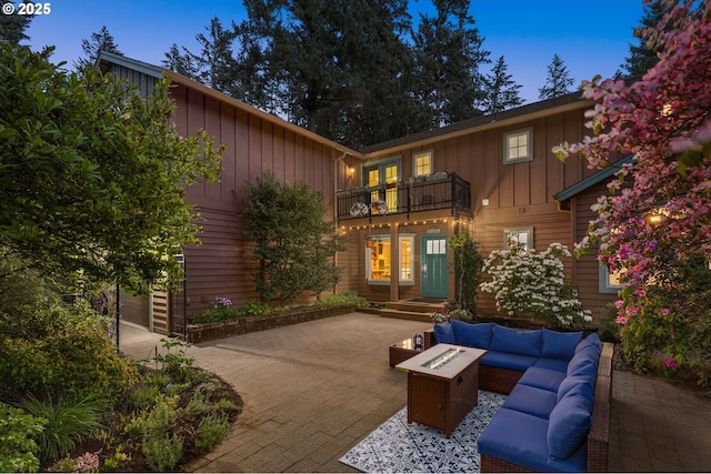 patio terrace at dusk with french doors, a balcony, and an outdoor living space with a fire pit