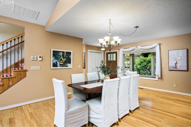 dining area featuring a notable chandelier, light wood finished floors, baseboards, visible vents, and stairway
