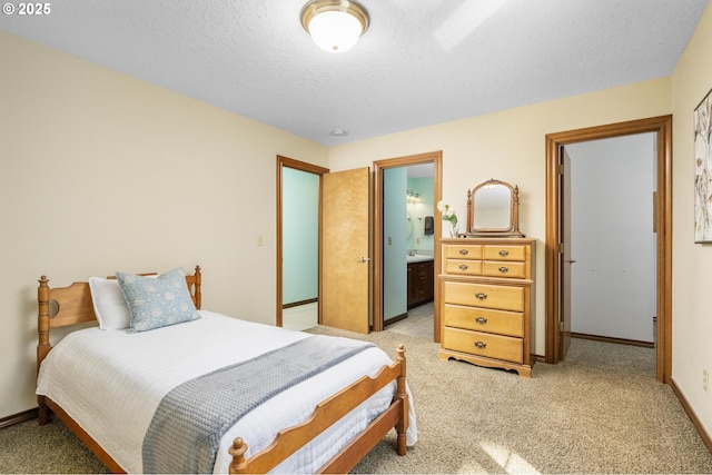 bedroom with a textured ceiling, light carpet, baseboards, and ensuite bath
