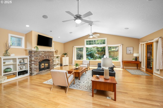 living room featuring a ceiling fan, a textured ceiling, a stone fireplace, vaulted ceiling, and light wood finished floors