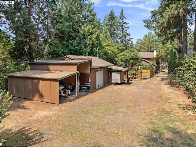 rear view of property with a garage, roof with shingles, fence, and driveway