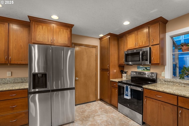 kitchen featuring recessed lighting, appliances with stainless steel finishes, brown cabinets, and light stone counters