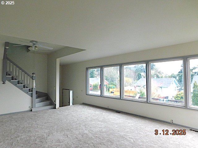 unfurnished living room with stairs, a ceiling fan, and carpet floors