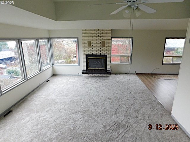 unfurnished living room with a ceiling fan, a brick fireplace, a healthy amount of sunlight, and visible vents