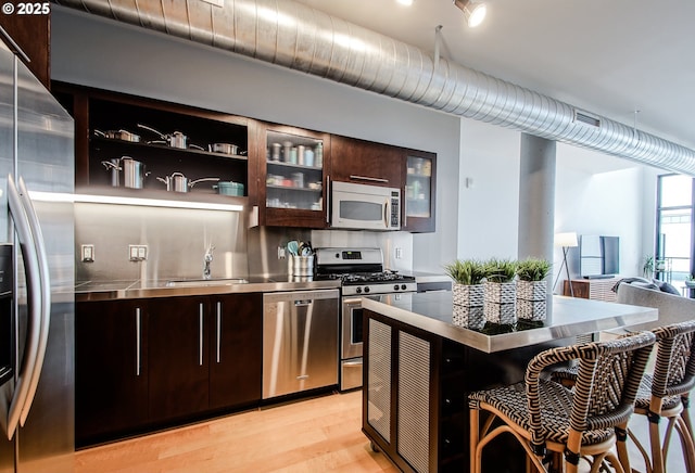 1400 NW Irving St Unit 715, Portland, OR 97209 - kitchen with stainless steel countertops, appliances with stainless steel finishes, a sink, dark brown cabinetry, and light wood-type flooring