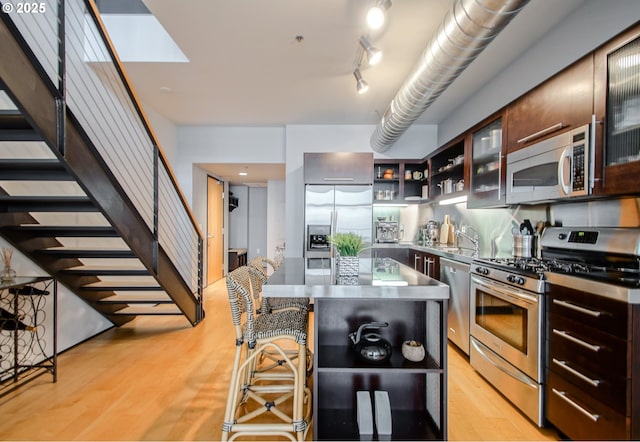 1400 NW Irving St Unit 715, Portland, OR 97209 - kitchen featuring stainless steel countertops, stainless steel appliances, open shelves, light wood finished floors, and glass insert cabinets