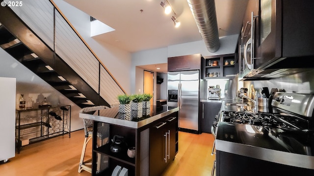 1400 NW Irving St Unit 715, Portland, OR 97209 - kitchen featuring stainless steel appliances, open shelves, stainless steel counters, dark cabinetry, and a kitchen island