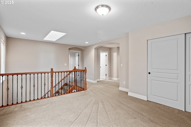 hall featuring a skylight, light colored carpet, and a textured ceiling