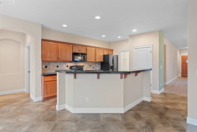 kitchen with a kitchen breakfast bar, tasteful backsplash, an island with sink, and black appliances