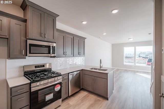 kitchen featuring sink, light hardwood / wood-style flooring, stainless steel appliances, tasteful backsplash, and kitchen peninsula