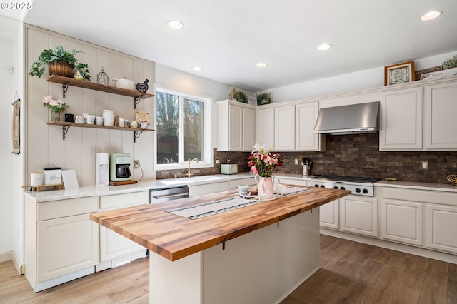 kitchen featuring gas cooktop, light wood-style flooring, butcher block counters, decorative backsplash, and wall chimney exhaust hood