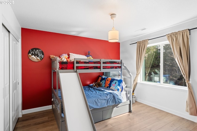 bedroom featuring an accent wall, visible vents, baseboards, and wood finished floors