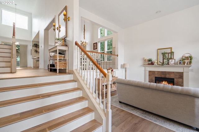 stairs featuring wood finished floors, a tile fireplace, a towering ceiling, and a notable chandelier