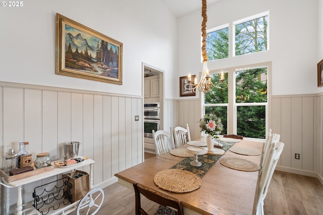 dining area with a chandelier, a wainscoted wall, a towering ceiling, and light wood finished floors