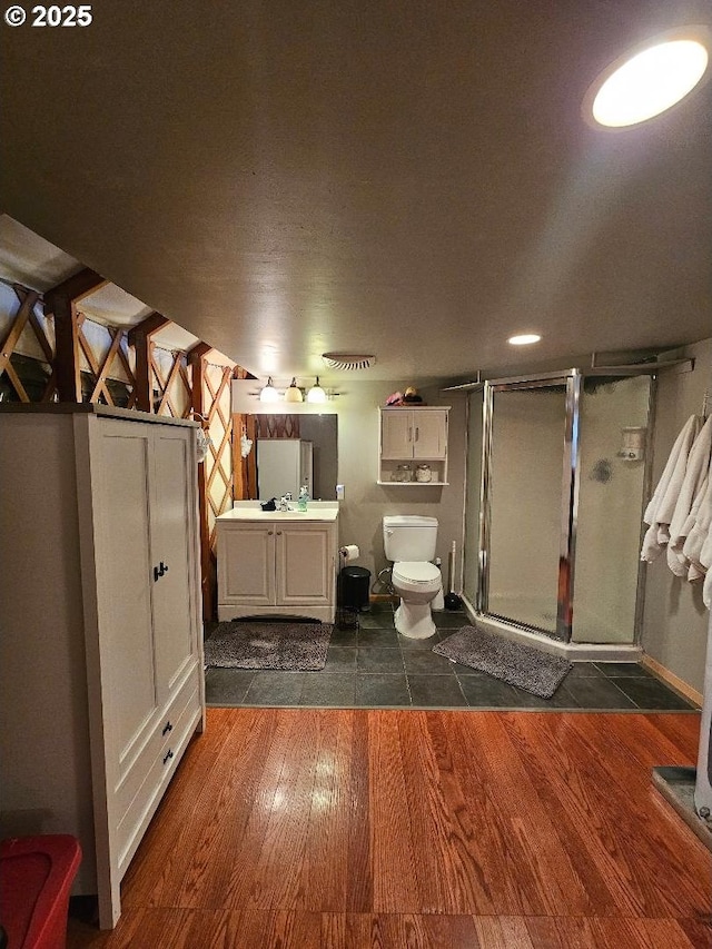 bathroom featuring wood finished floors, a stall shower, toilet, and vanity