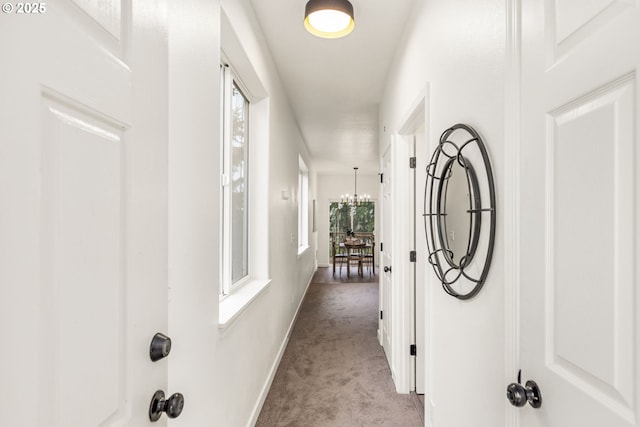 hallway with a chandelier, carpet, and baseboards