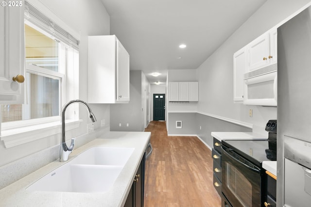 kitchen with black electric range, white microwave, a sink, freestanding refrigerator, and white cabinets