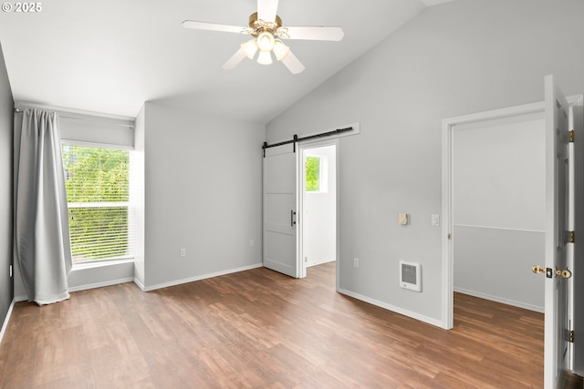 spare room with a barn door, healthy amount of natural light, wood finished floors, and vaulted ceiling