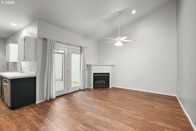 unfurnished living room with a sink, wood finished floors, a ceiling fan, baseboards, and a fireplace