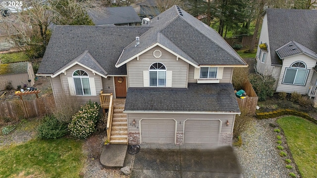 view of front of home featuring driveway, a shingled roof, a garage, and fence