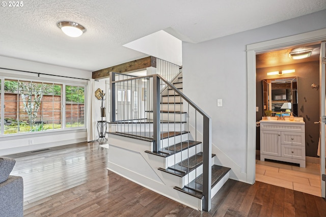 staircase featuring baseboards, a textured ceiling, visible vents, and wood finished floors