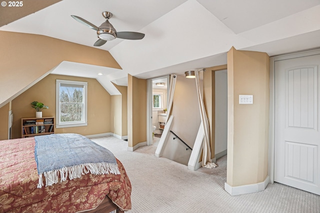 carpeted bedroom featuring vaulted ceiling, ensuite bathroom, a ceiling fan, and baseboards