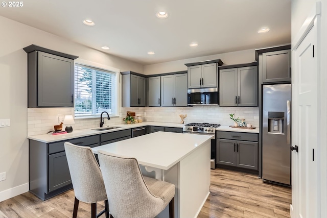 kitchen featuring sink, gray cabinets, appliances with stainless steel finishes, a kitchen island, and a kitchen bar