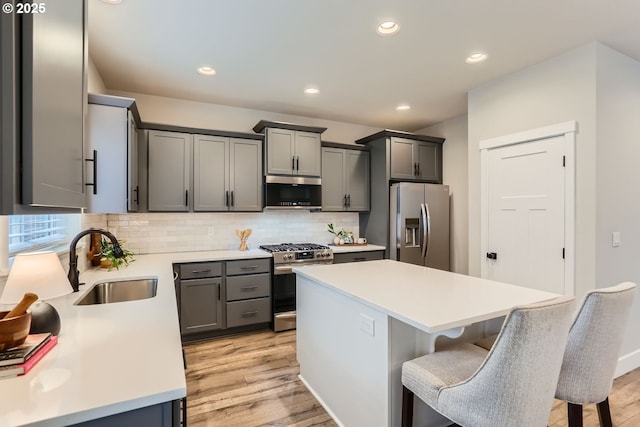 22410 SW Forest Creek Way, Sherwood, OR 97140 - kitchen with appliances with stainless steel finishes, a sink, light wood-style floors, backsplash, and light countertops