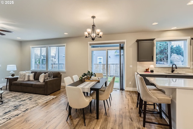 dining area with sink, ceiling fan with notable chandelier, and light hardwood / wood-style floors