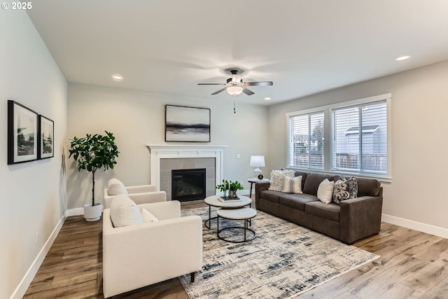 living room with ceiling fan, wood-type flooring, and a tile fireplace