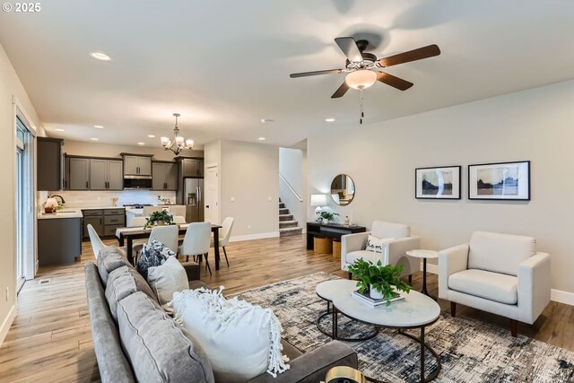 living room featuring sink, ceiling fan with notable chandelier, and light wood-type flooring