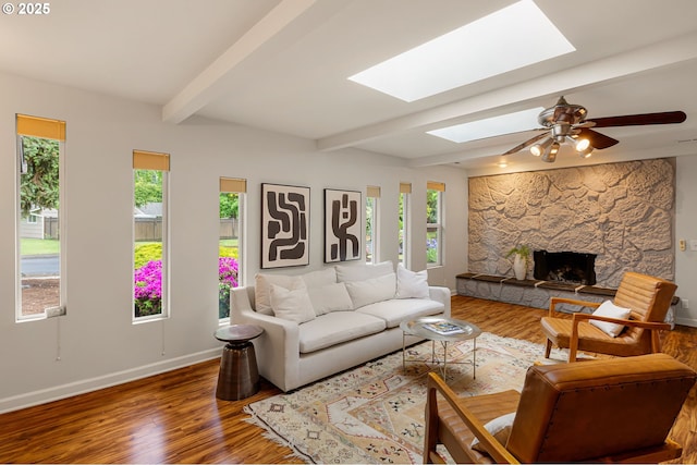 living room with a skylight, plenty of natural light, wood finished floors, beam ceiling, and baseboards