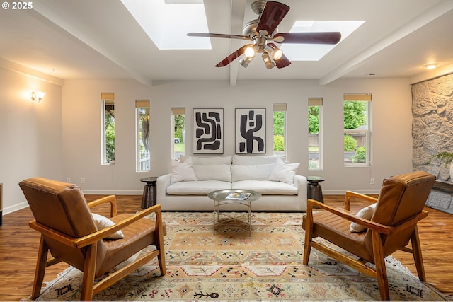 living room featuring a skylight, wood finished floors, baseboards, and ceiling fan